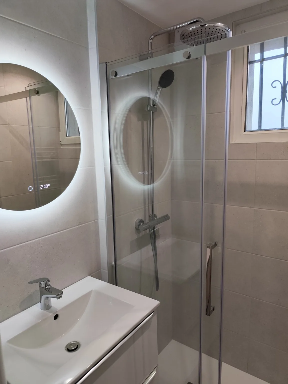 Petite salle de bains avec douche, vasque et miroir éclairé