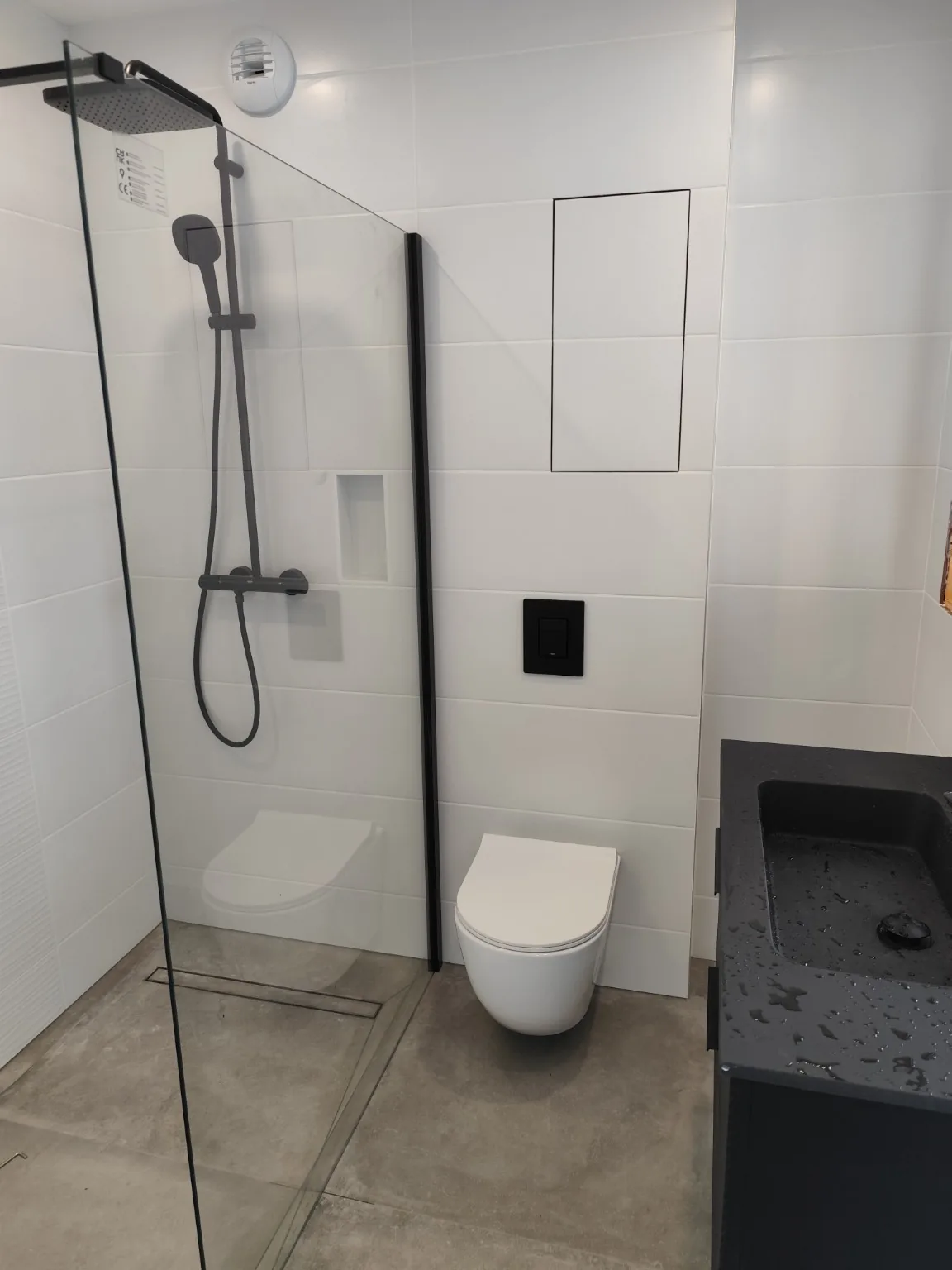 Salle de bains blanche et noire avec douche à l’italienne et WC suspendu